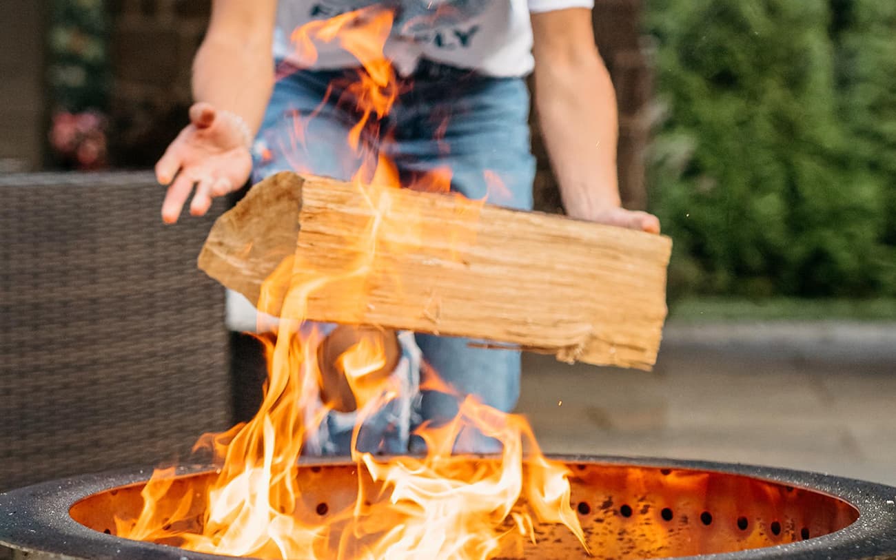 Hands throwing wood into a Breeo fire pit